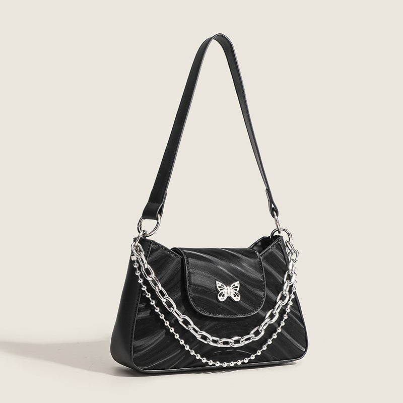 Kleine trapezförmige Schultertasche mit welliger Lederoptik, silberfarbenem Schmetterlingsverschluss vorne und mehrlagigem Kettenriemen mit Kugeldetails