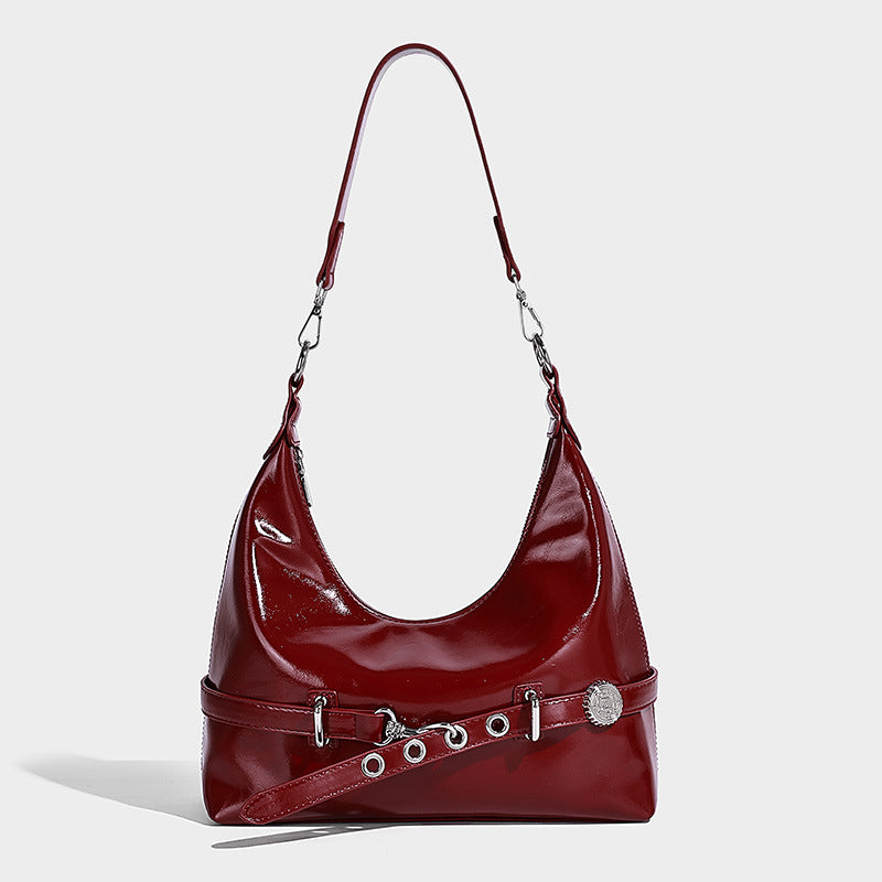 Glossy black slouchy hobo shoulder bag with silver-tone hardware, belt-style grommet strap at base, and long adjustable