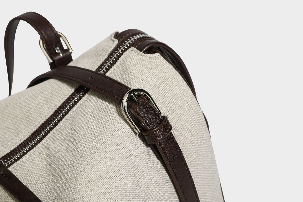 Beige canvas barrel bag with dark brown leather-look trim, silver-tone hardware, top zip closure, and adjustable shoulder