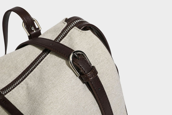 Beige canvas barrel bag with dark brown leather-look trim, silver-tone hardware, top zip closure, and adjustable shoulder
