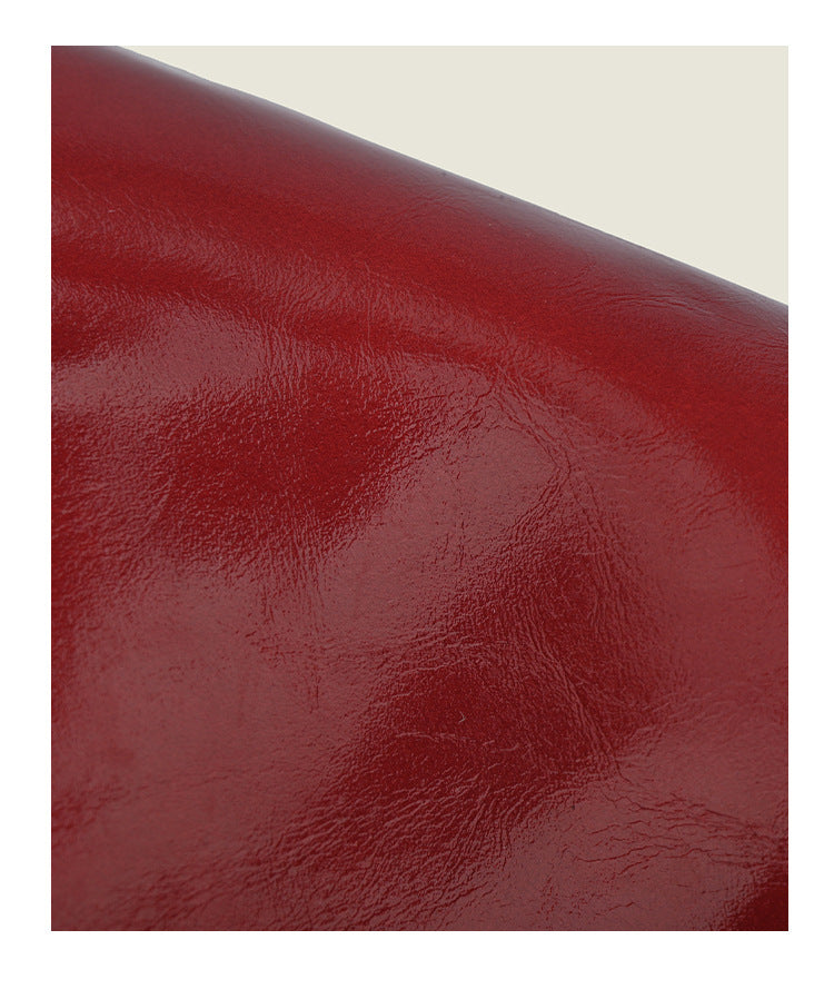 Small structured red glossy PU handbag with bow-and-bead charm, dual top handles, and detachable crossbody strap, detail view