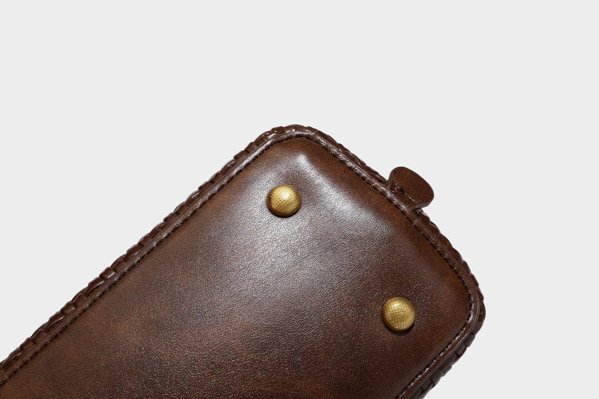 Structured woven-embossed leather-look satchel with dual rolled top handles, gold-tone turn-lock closure, and detachable