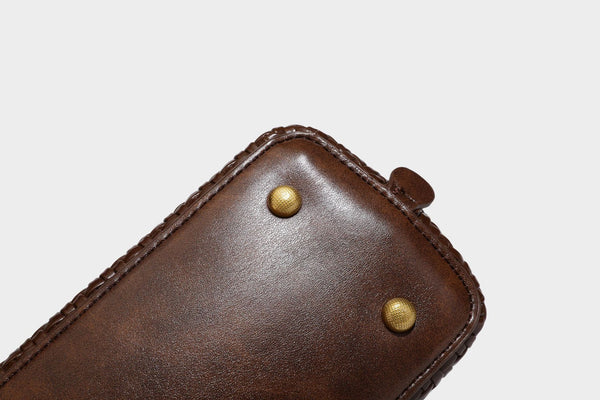 Structured woven-embossed leather-look satchel with dual rolled top handles, gold-tone turn-lock closure, and detachable