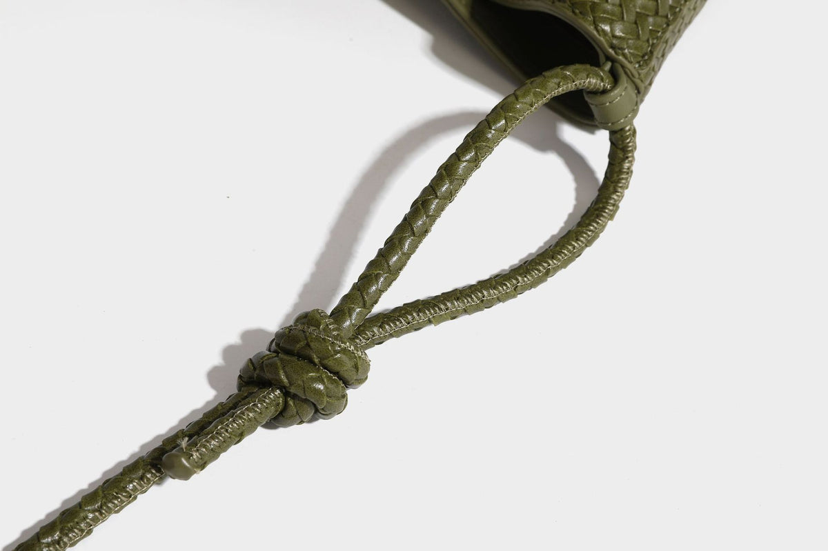 Olive green woven leather-look bucket bag with braided crossbody strap, knotted adjustment, and gold-tone tassel charm with