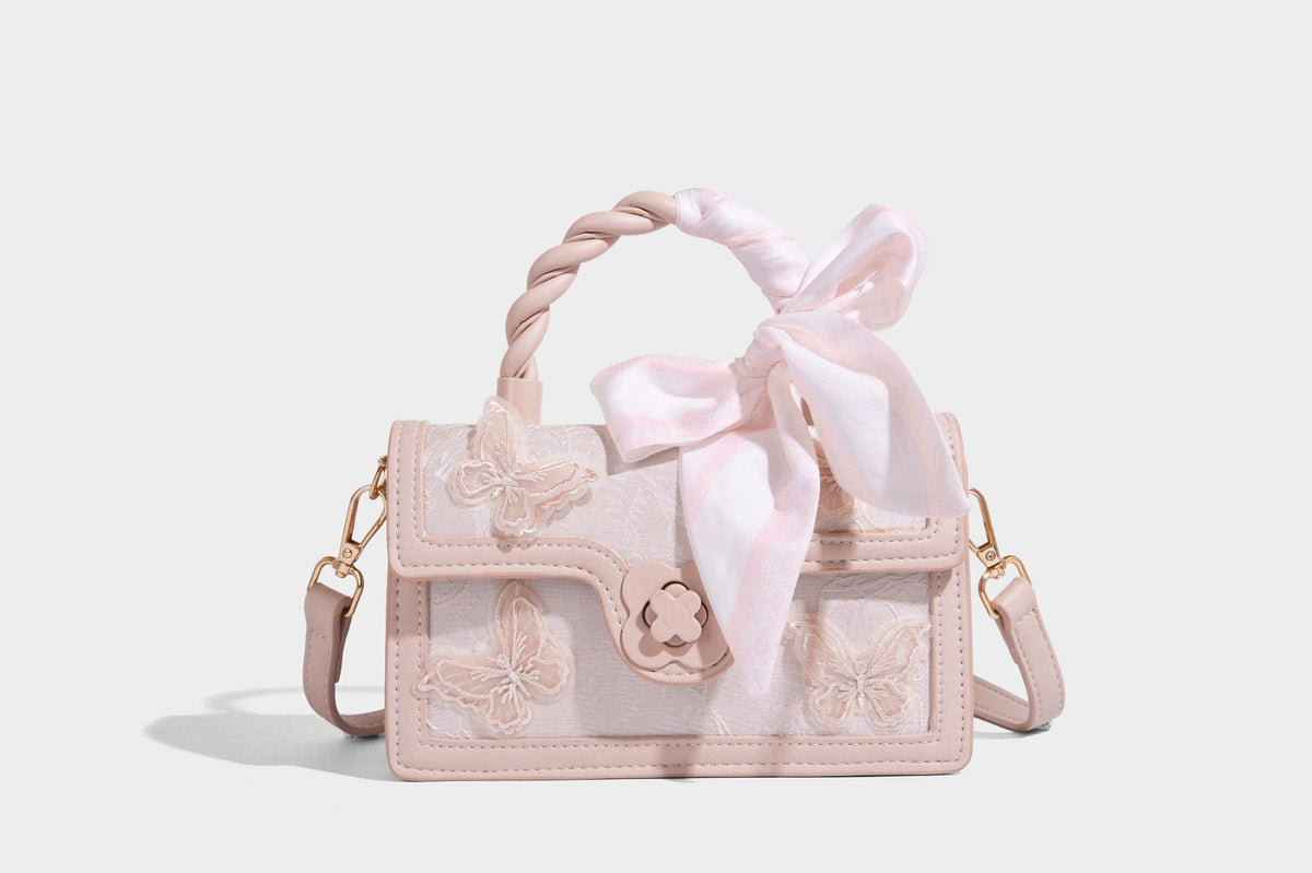 Small structured white flap bag with butterfly embroidery, flower-shaped turn-lock clasp, braided top handle with scarf bow