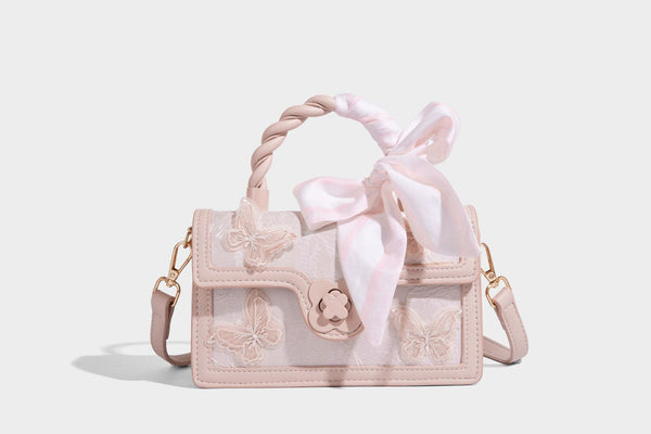Small structured white flap bag with butterfly embroidery, flower-shaped turn-lock clasp, braided top handle with scarf bow