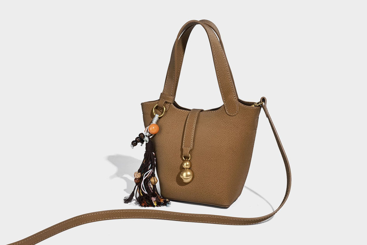 Kleine matte Beuteltasche mit genarbter Oberfläche, antikgoldfarbenen Ringbeschlägen, Perlen- und Quastenanhänger, kurzen Tragegriffen oben und