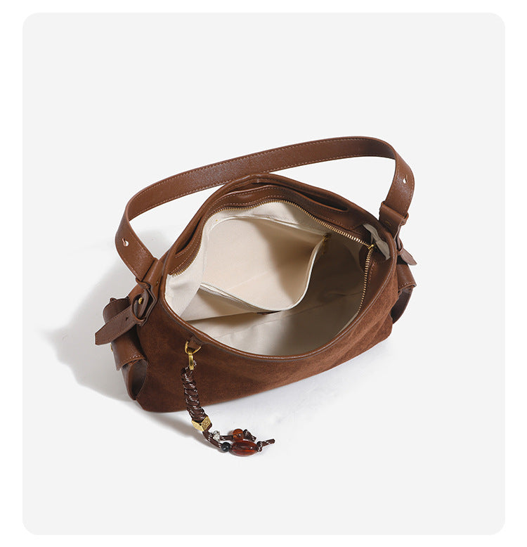 Caramel brown slouchy hobo shoulder bag with matte suede-like finish, braided tassel charm, brass-tone hardware, and, detail