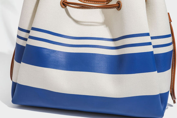 Large cream and navy striped canvas bucket tote bag with tan leather-look trim, drawstring closure, and double shoulder