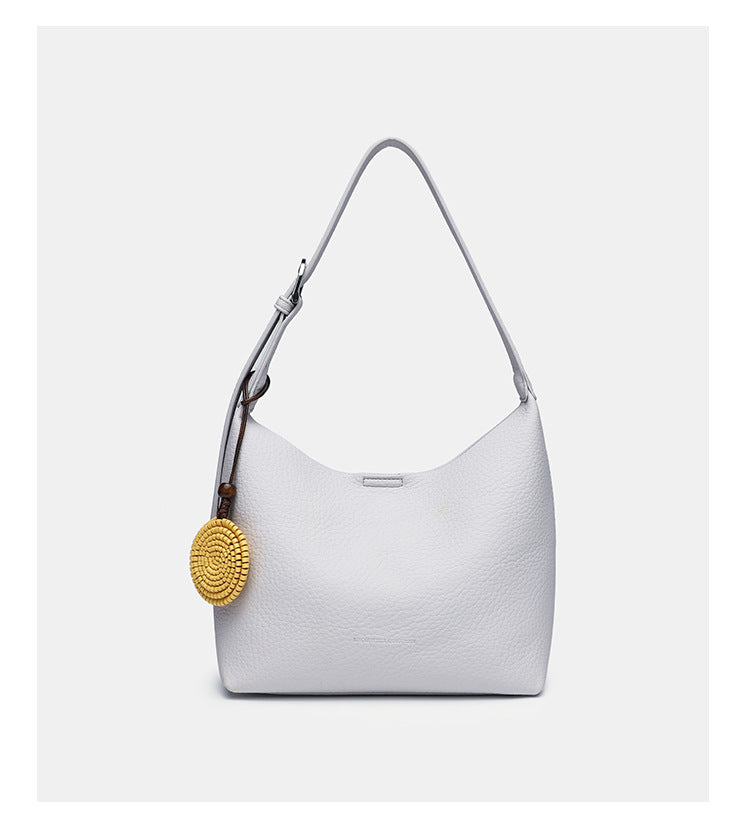 Slouchy hobo shoulder bag in pale yellow pebbled texture with woven charm, adjustable strap, matching zip pouch, and, detail