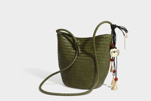 Olive green woven leather-look bucket bag with braided crossbody strap, knotted adjustment, and gold-tone tassel charm with
