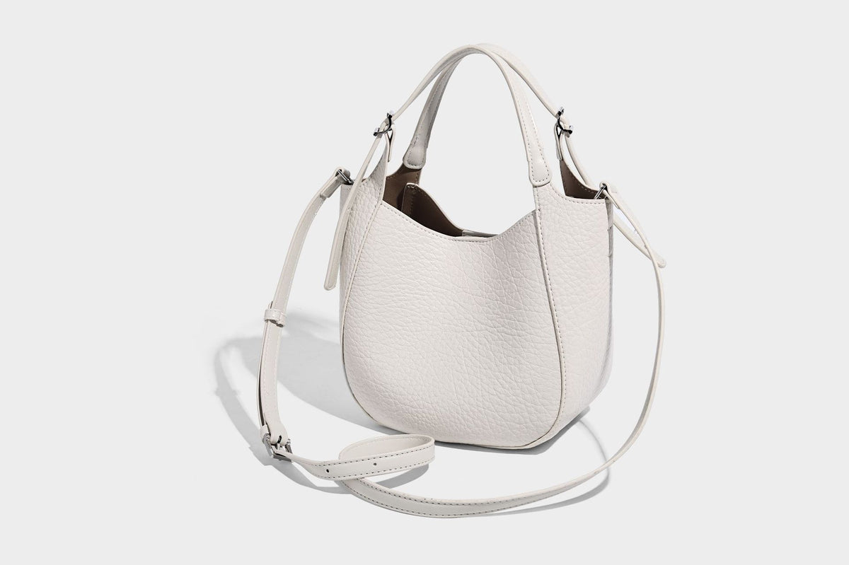 Small pebbled half-moon shoulder bag with dual top handles, detachable crossbody strap, and silver-tone hardware, detail view