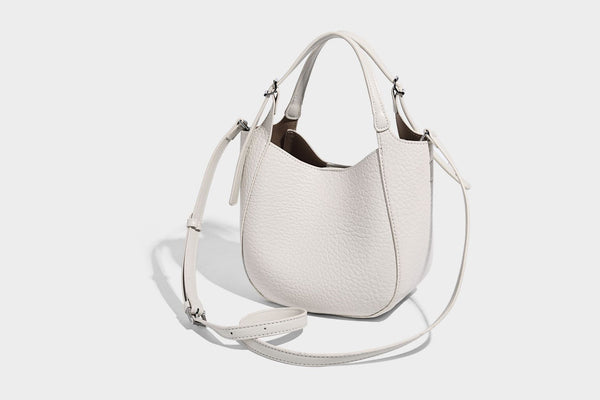 Small pebbled half-moon shoulder bag with dual top handles, detachable crossbody strap, and silver-tone hardware, detail view