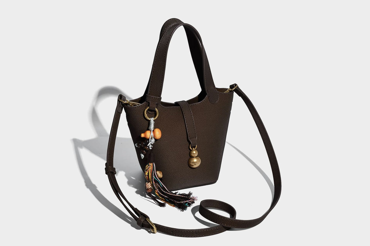 Kleine matte Beuteltasche mit genarbter Oberfläche, antikgoldfarbenen Ringbeschlägen, Perlen- und Quastenanhänger, kurzen Tragegriffen oben und