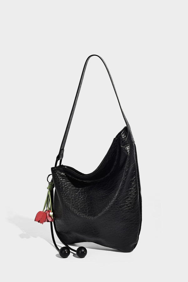 Slouchy hobo shoulder bag in pale yellow with slim strap, drawstring bead closure, and pink tulip floral charm, detail view