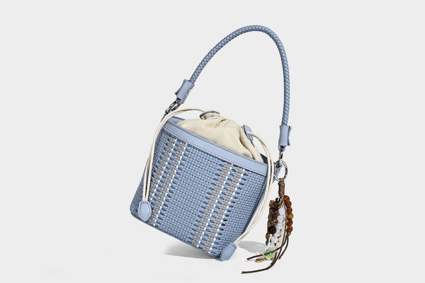Small woven bucket bag with drawstring top, braided handle, detachable crossbody strap, and silver-tone ring hardware, detail