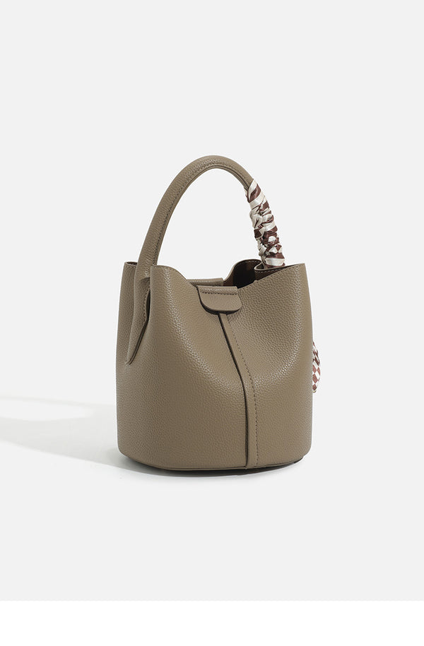 Pebbled leather-look bucket bag with checkered scarf-wrapped top handle, flap tab closure, gold-tone hardware, and matching