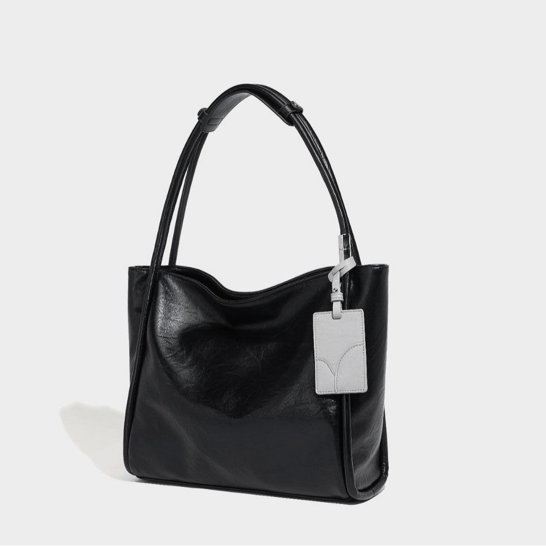 Black glossy leather-look tote bag with twin round top handles and silver-tone hardware, detail view 2