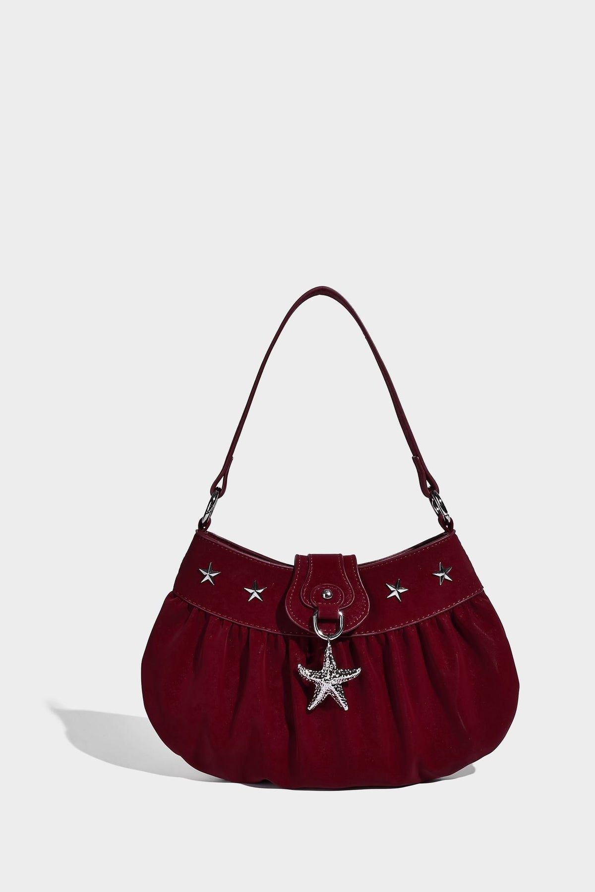 Ruched shoulder bag with curved flap, silver star studs, dangling starfish charm, and adjustable crossbody strap, detail view