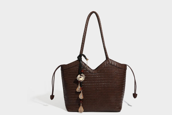 Olivgrüne Tote-Bag in Korbgeflecht-Optik mit dunkelbraunen geflochtenen Schulterriemen, seitlichen Kordelzügen und Perlenanhänger in Goldoptik