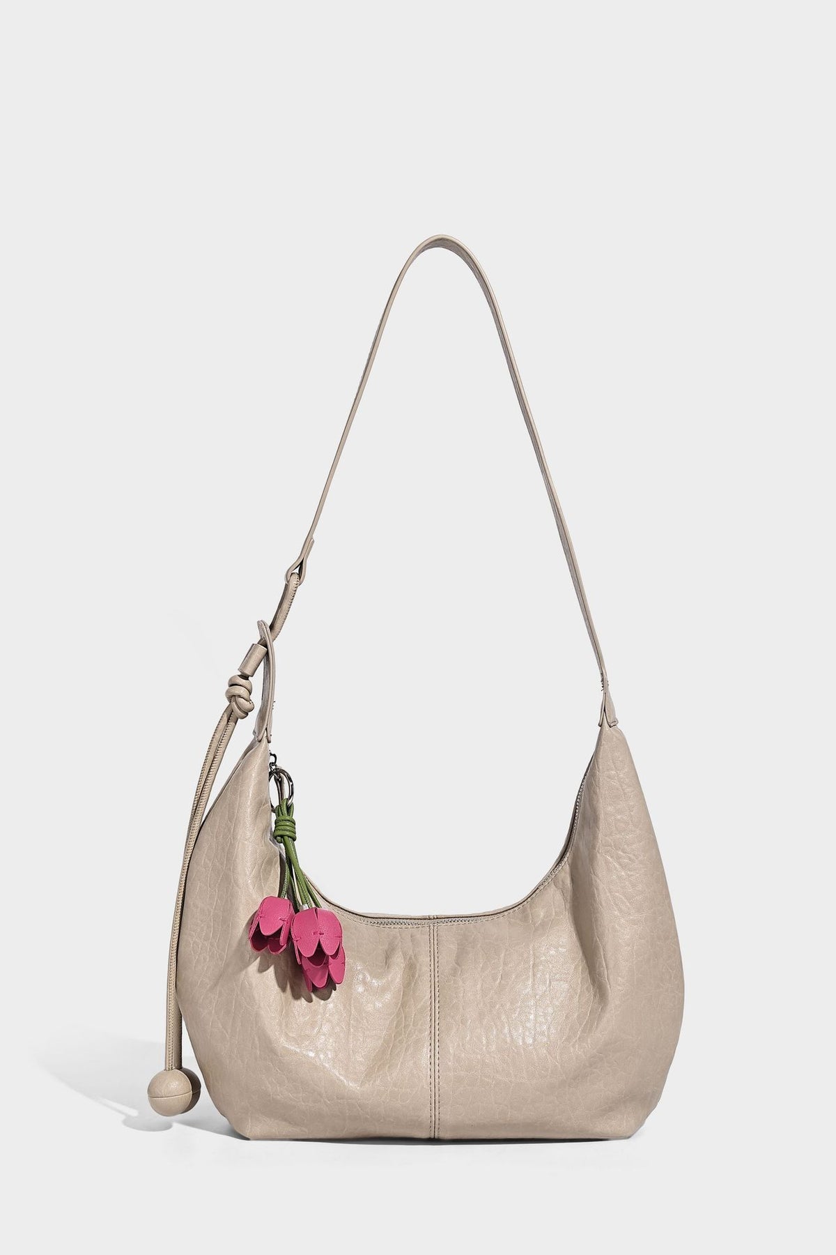Slouchy crescent half-moon shoulder bag in pink pebbled textured finish with floral charm and knotted side detail, detail