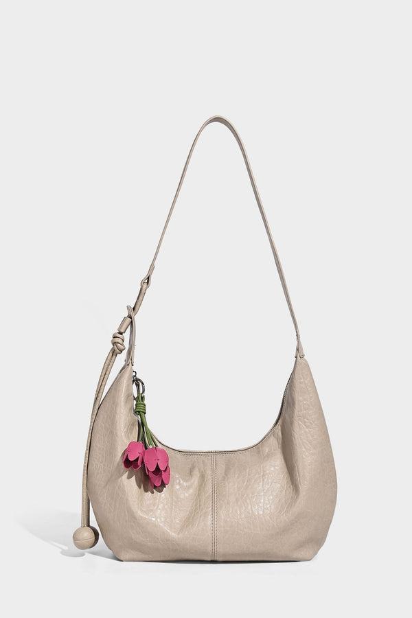 Slouchy crescent half-moon shoulder bag in pink pebbled textured finish with floral charm and knotted side detail, detail