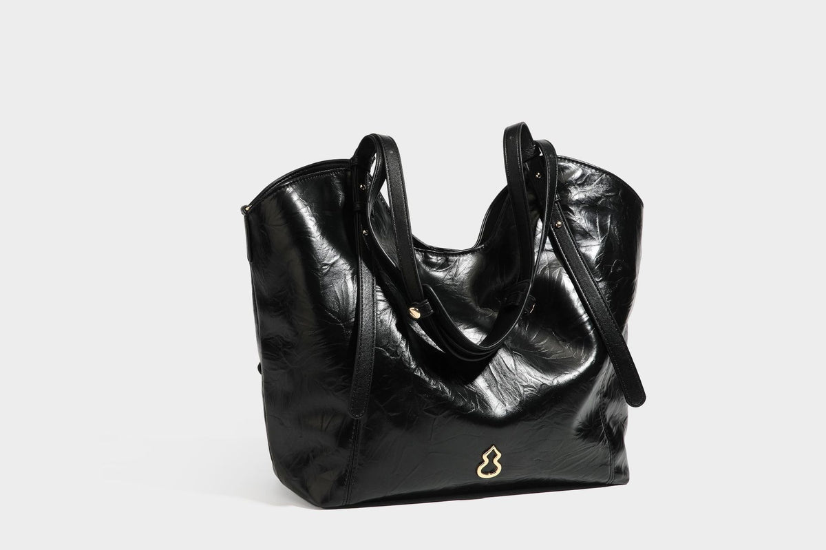 Große, glänzende Tote-Bag aus schwarzem Lederimitat mit geknitterter Optik, lässig fallender Trapezsilhouette, zwei Schulterriemen und goldfarbenen