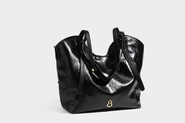 Große, glänzende Tote-Bag aus schwarzem Lederimitat mit geknitterter Optik, lässig fallender Trapezsilhouette, zwei Schulterriemen und goldfarbenen