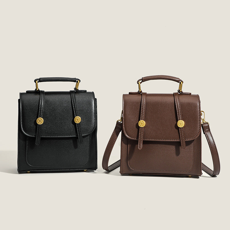 Structured mini satchel backpack with smooth leather-look finish, front flap pocket, gold-tone stud closures, and top handle