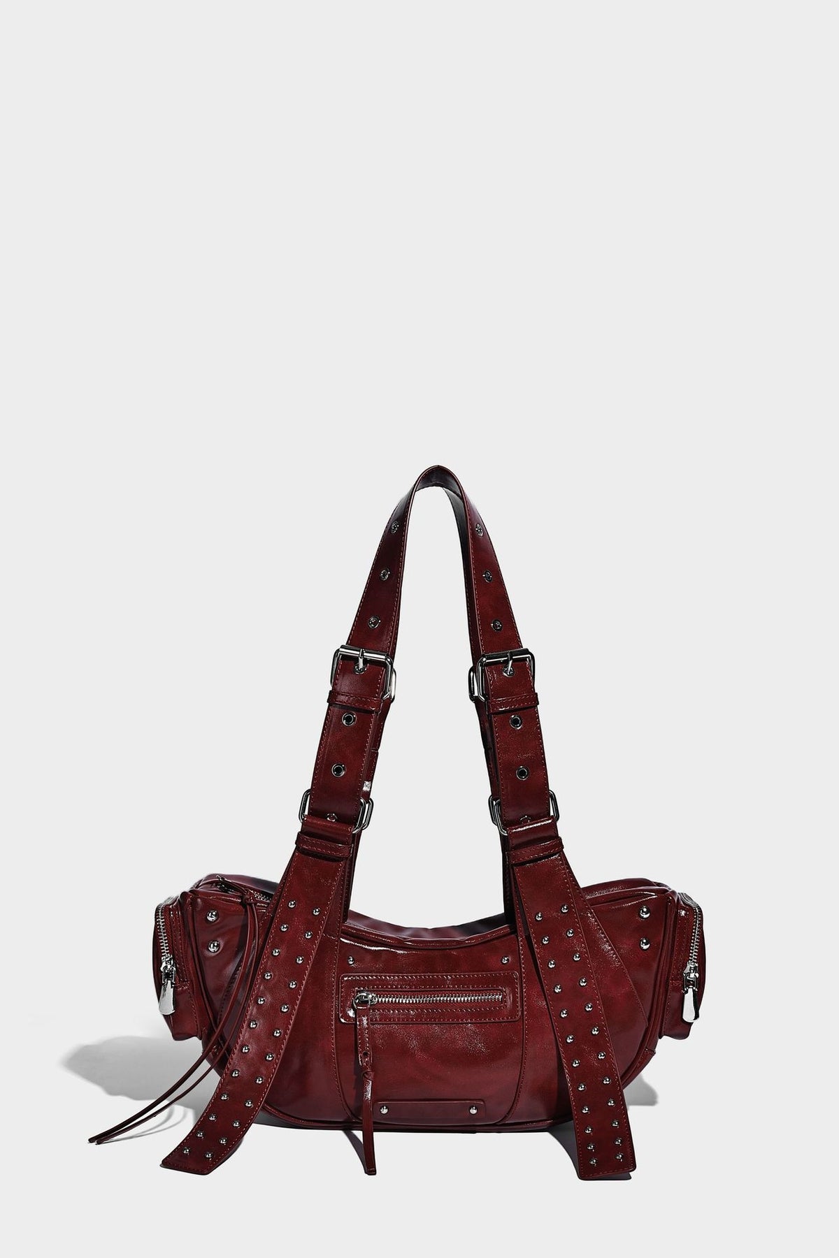 Glossy black crescent shoulder bag with silver-tone rivets, multiple zip pockets, and long adjustable studded straps, detail