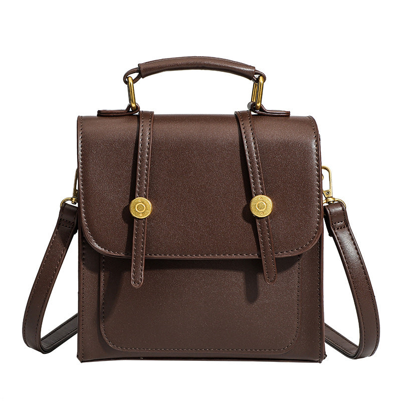 Structured mini satchel backpack with smooth leather-look finish, front flap pocket, gold-tone stud closures, and top handle