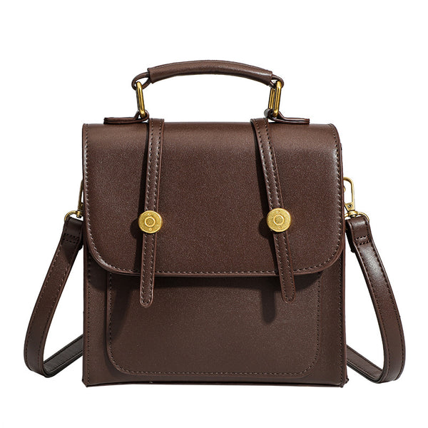 Structured mini satchel backpack with smooth leather-look finish, front flap pocket, gold-tone stud closures, and top handle