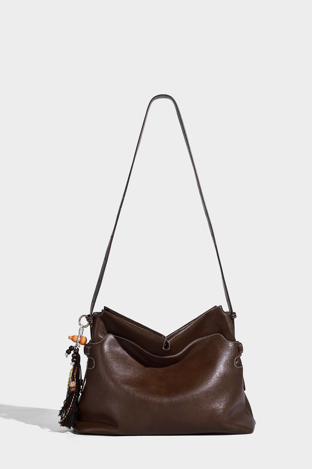 Large slouchy leather-look hobo tote bag with open top, adjustable shoulder strap, and colorful tassel bead charm, detail