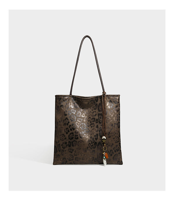 Large leopard print shoulder tote bag in tan and brown with slim dark straps and dangling beaded charm hardware, detail view