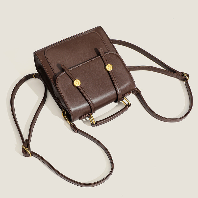 Structured mini satchel backpack with smooth leather-look finish, front flap pocket, gold-tone stud closures, and top handle