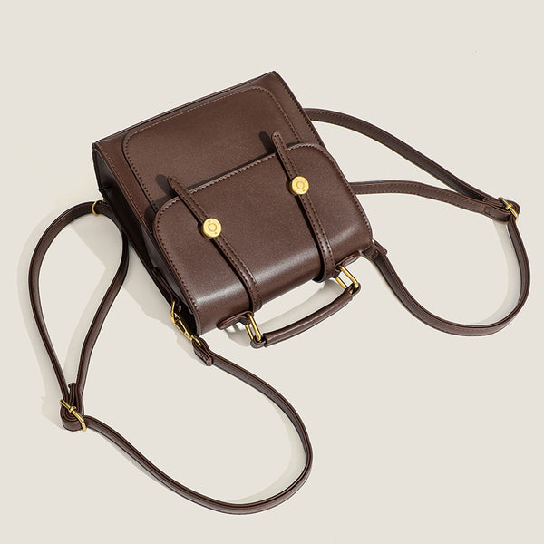Structured mini satchel backpack with smooth leather-look finish, front flap pocket, gold-tone stud closures, and top handle