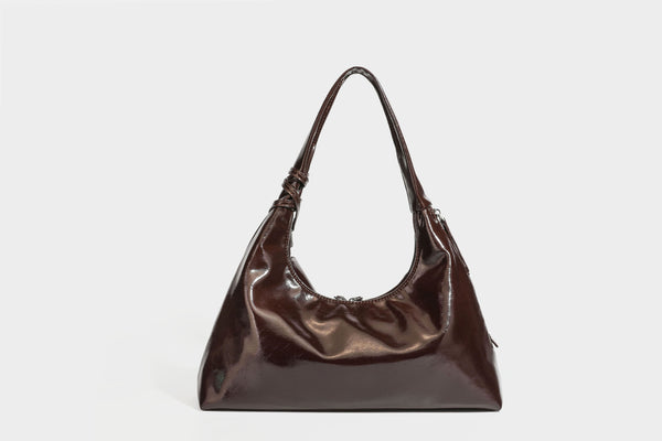 Weich fallende Hobo-Schultertasche in glänzender Lederoptik mit silberfarbenen Ösen zum Schnüren und Schleifenband auf der Vorderseite, Detailansicht