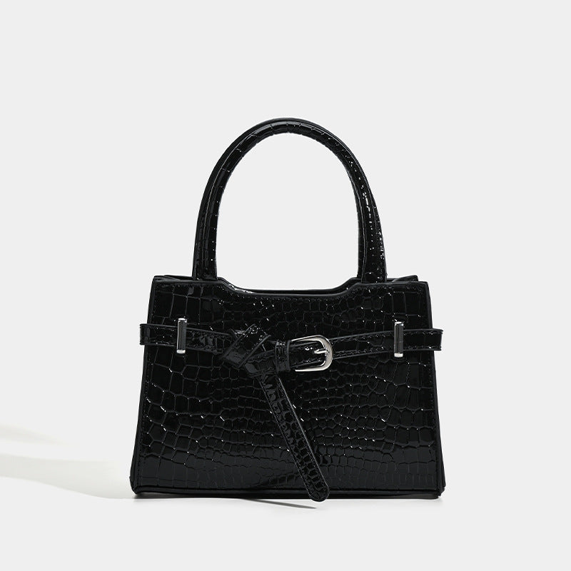 Small structured trapezoid mini top-handle bag with front belt-knot buckle detail and glossy leather-look finish, detail view