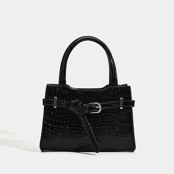 Small structured trapezoid mini top-handle bag with front belt-knot buckle detail and glossy leather-look finish, detail view