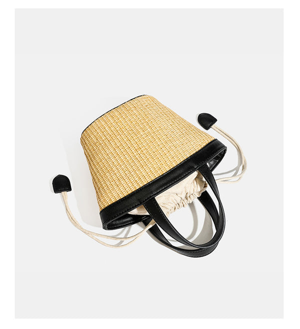 Kleine geflochtene Bucket Bag aus Stroh mit schwarzem Besatz in Lederoptik, zwei oberen Tragegriffen, cremefarbenem Futter mit Kordelzug und seitlichen Kordelverschlüssen