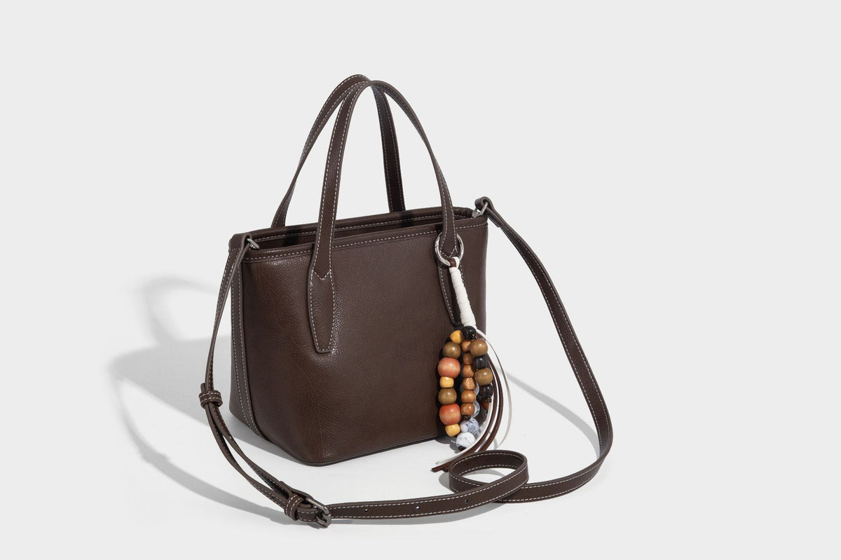 Compact structured bucket tote bag with pebbled textured finish, dual top handles, silver-tone lock hardware, and detachable