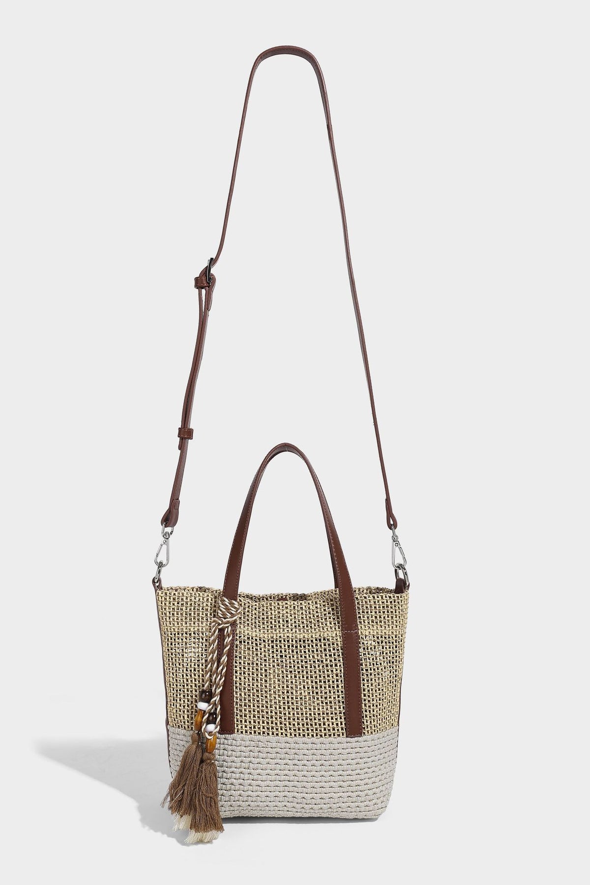 Two-tone open-weave tote bag in beige and cream with brown leather-look handles, tassel bead charm, and detachable