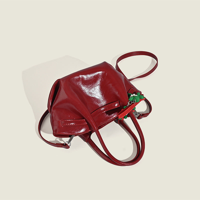 Small structured red glossy PU handbag with bow-and-bead charm, dual top handles, and detachable crossbody strap, detail view