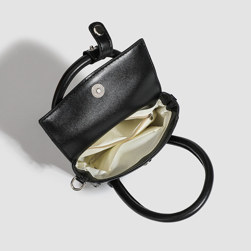 Kleine strukturierte schwarze Henkeltasche im Lederlook mit zwei abgerundeten Henkeln, abnehmbarem Umhängeriemen und silberfarbenem
