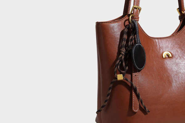 Structured smooth leather-look tote bag with long shoulder strap, gold-tone hardware, and hanging tassel-coin charm, detail