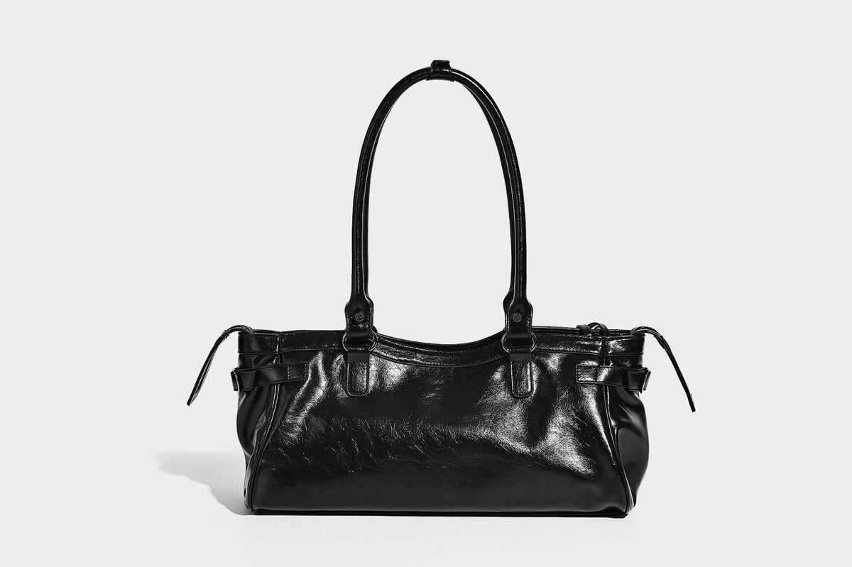 Längliche Schultertasche in Zylinderform mit glänzender Lederoptik, silberfarbenen Nietenbeschlägen, seitlichen Quasten und mehreren außenliegenden Reißverschlüssen