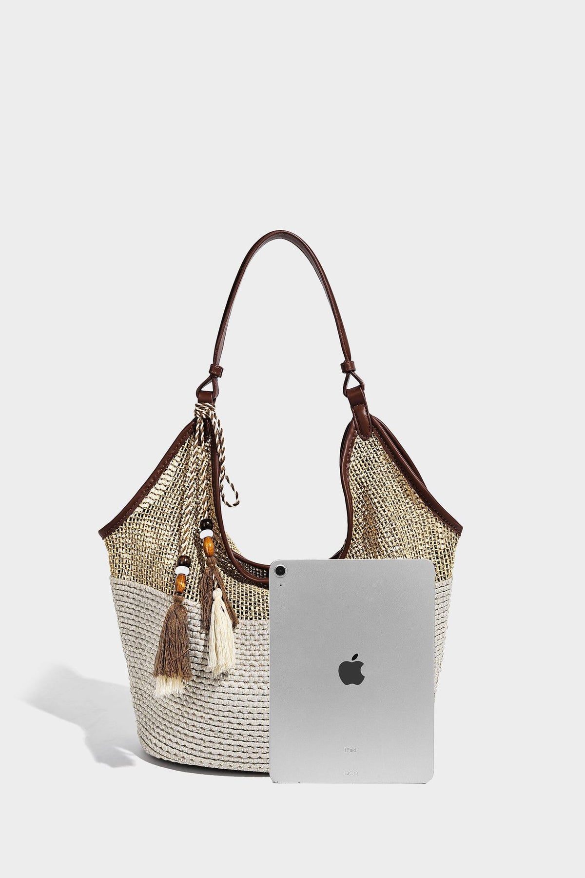 Two-tone beige and cream woven straw hobo shoulder bag with brown leather-look trim, long shoulder strap, and tassel-bead