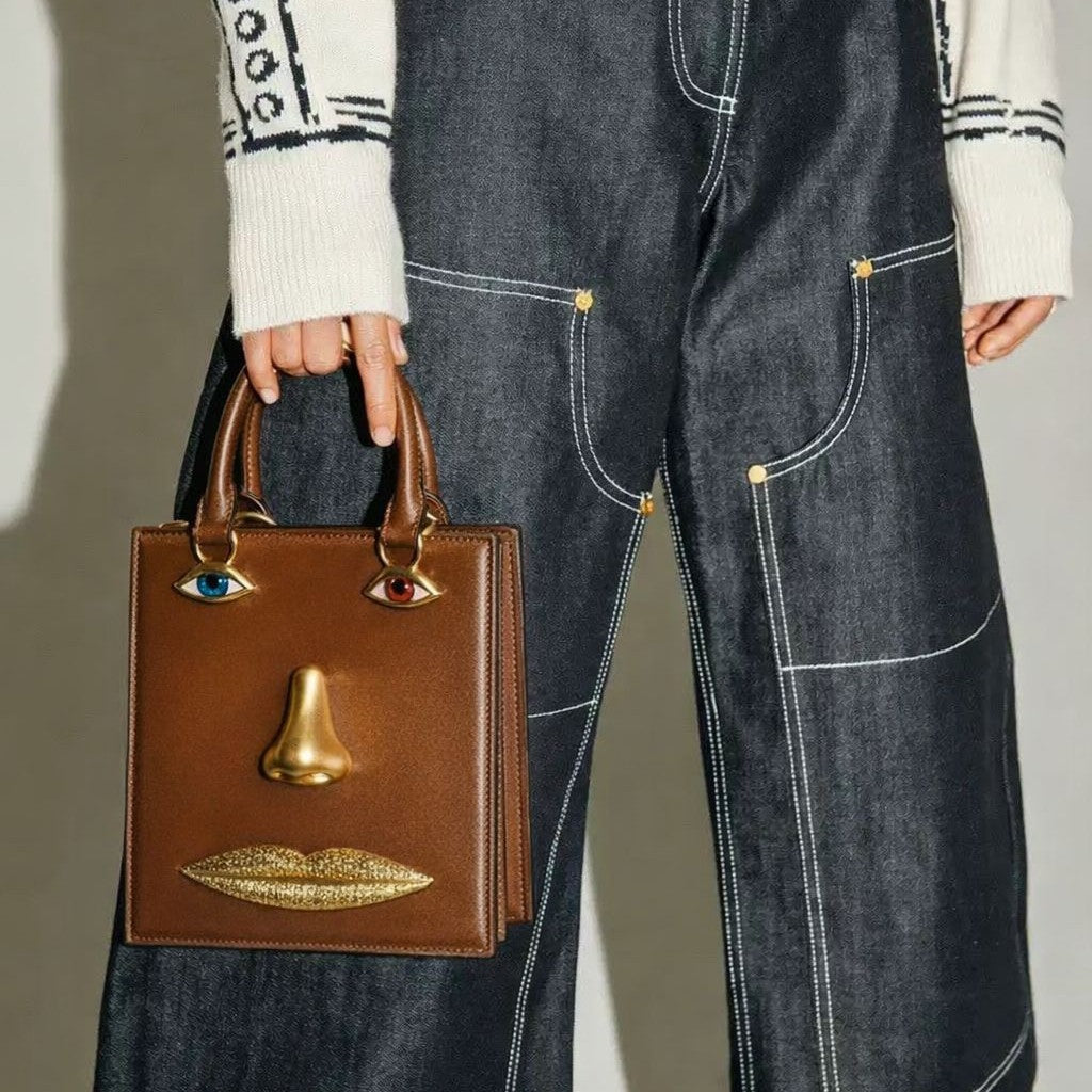 Structured rectangular top-handle bag in tan leather-look finish with gold-tone sculptural face hardware including