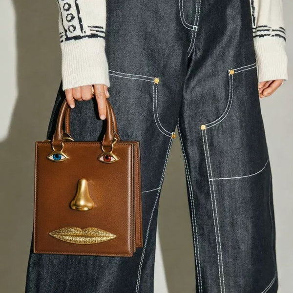 Structured rectangular top-handle bag in tan leather-look finish with gold-tone sculptural face hardware including