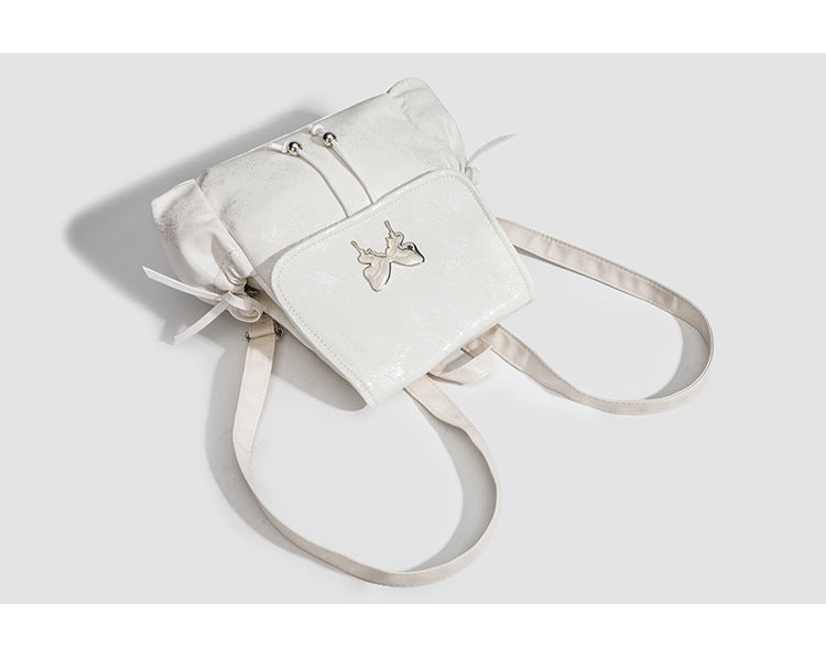 Compact white pearlescent flap backpack with silver-tone bow hardware and drawstring closure, detail view 7